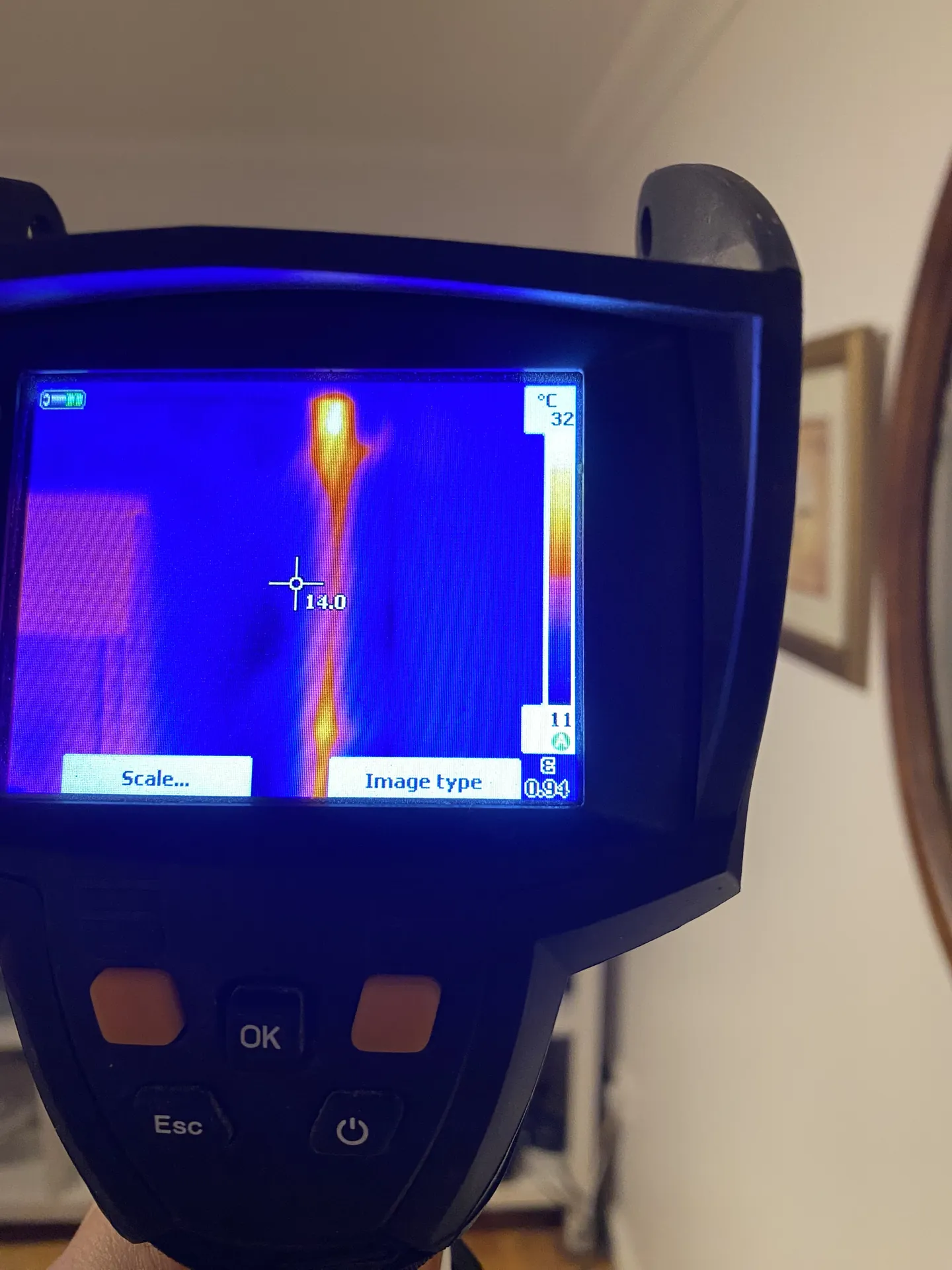 Thermal imaging camera screen showing a hot water pipe glowing inside a wall