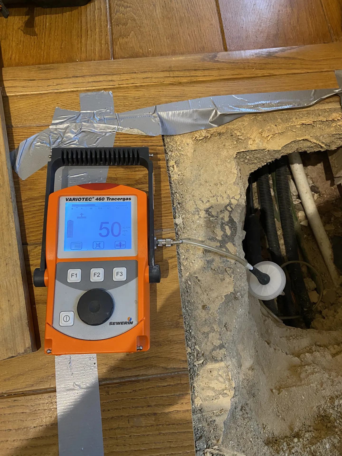 Tracer gas detector on a lifted floorboard with the pipe exposed between the joists